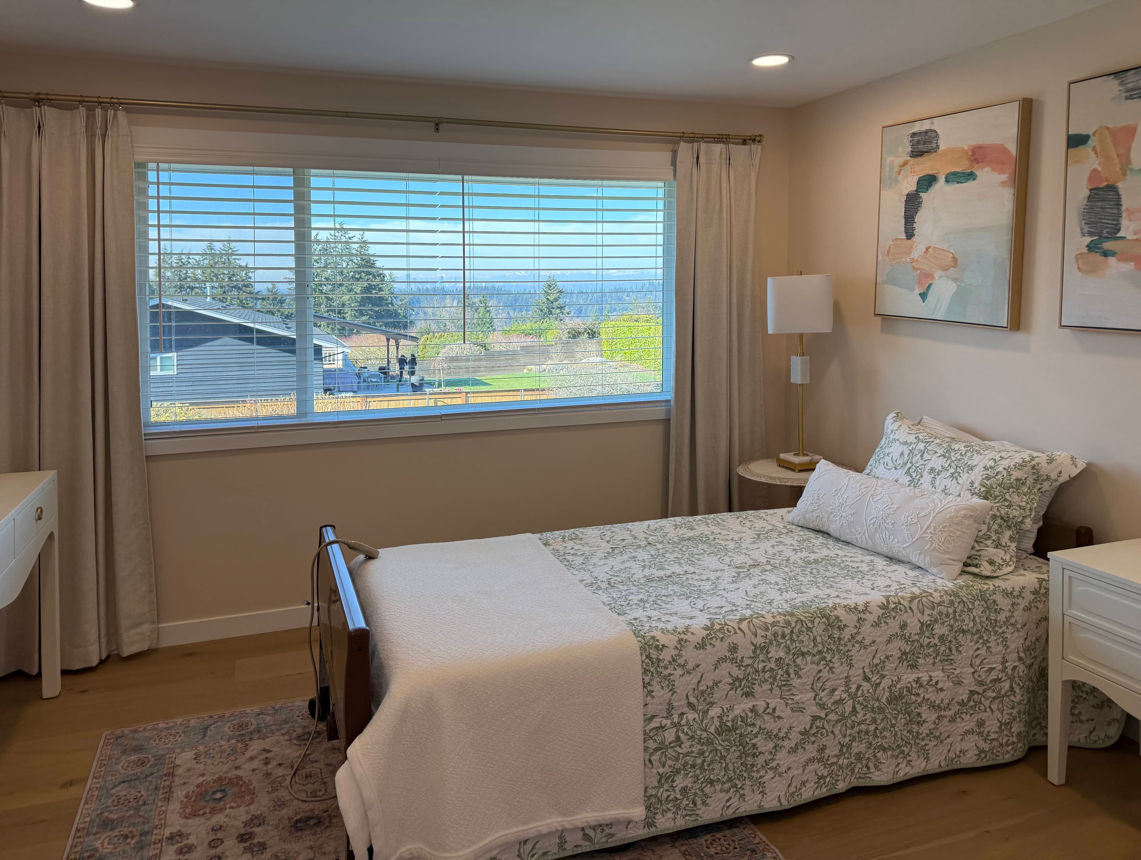 Bedroom with a single bed, floral linens, and large windows opening to a distant view.