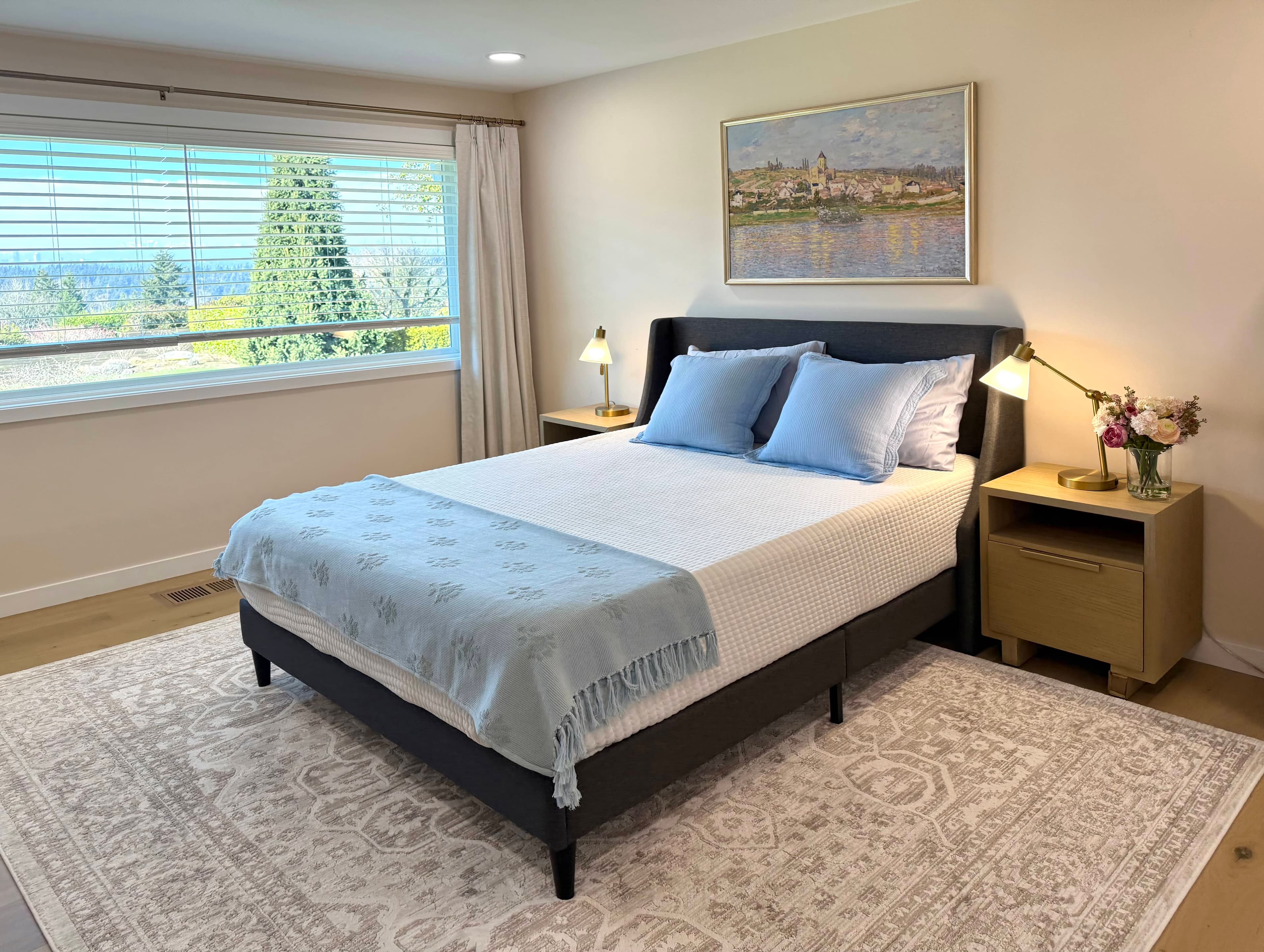 Bedroom at Norwood House with warm bedding, framed artwork, and a wood dresser in soft daylight.